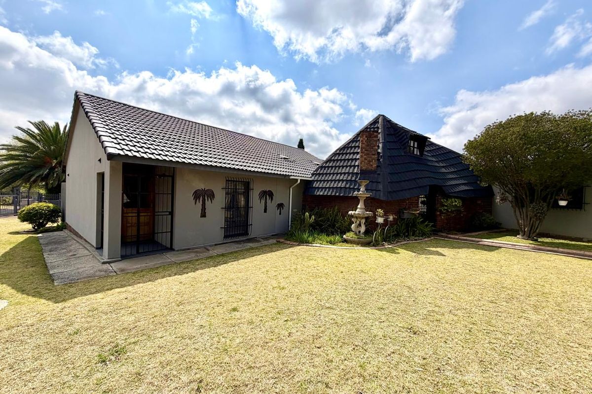 Rear view of the property featuring a well-maintained lawn, a stone fountain, and a combination of modern rendered walls and traditional brickwork with tiled roofing.