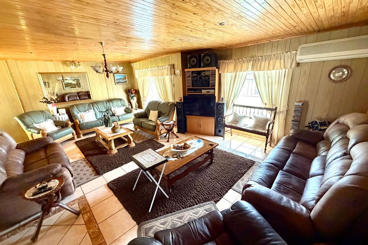 Spacious living room featuring timber-paneled walls and ceiling, ceramic tiled flooring, and a wall-mounted split system air conditioner.