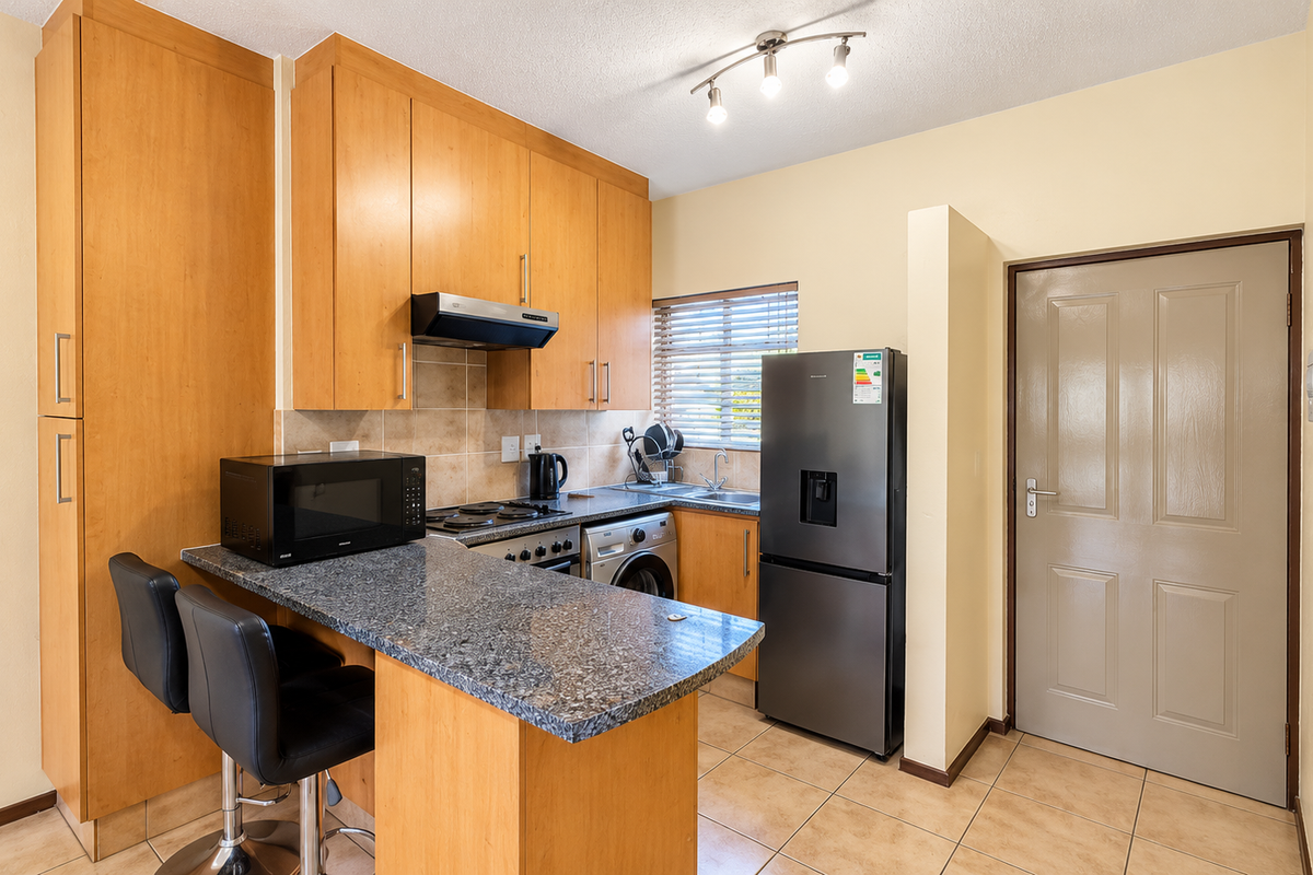 A functional kitchen featuring light wood cabinetry, granite countertops with a breakfast bar, tiled backsplash, and integrated appliances.
