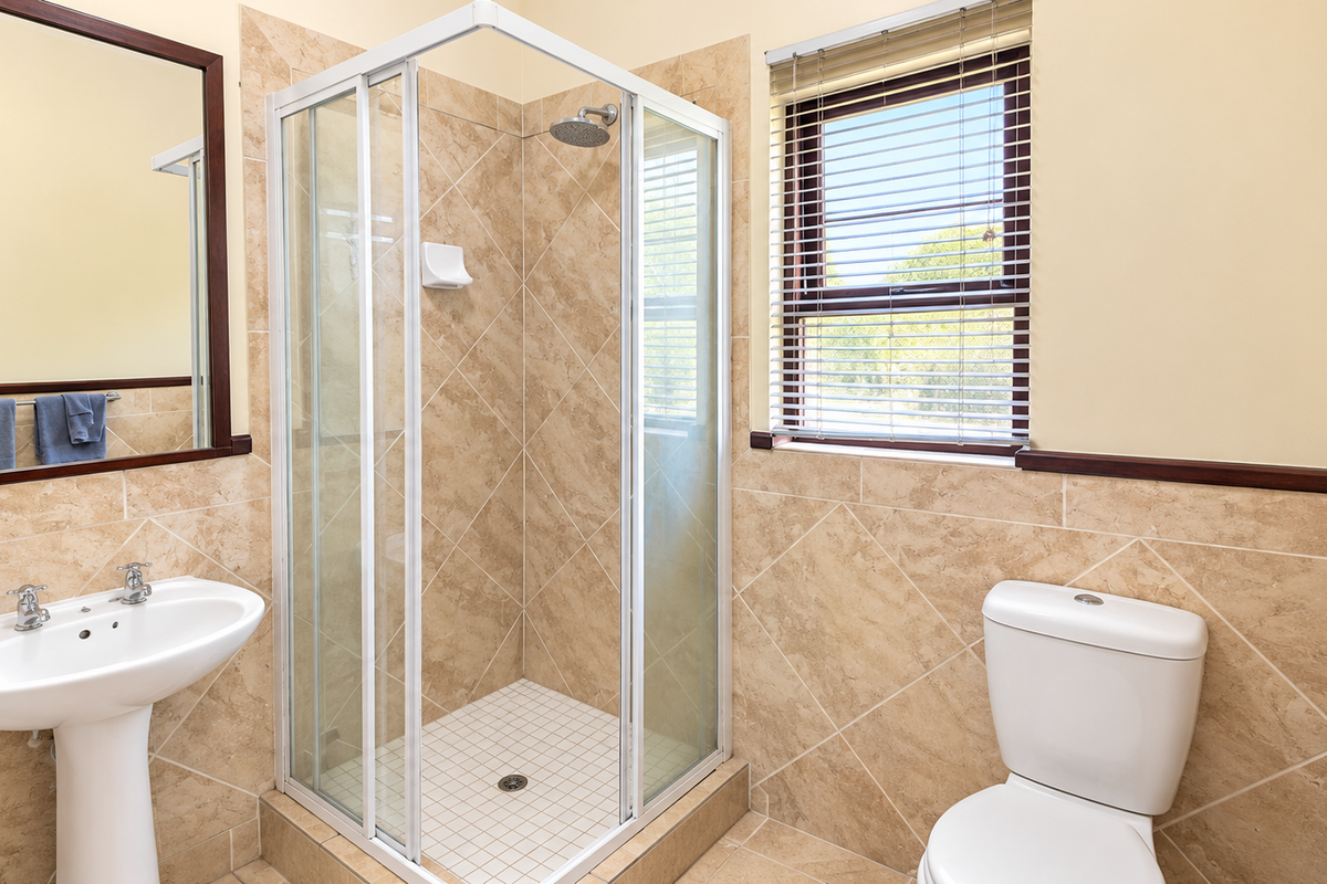 A clean and functional bathroom featuring a pedestal basin, a corner shower enclosure, and a toilet, finished with neutral wall and floor tiling.