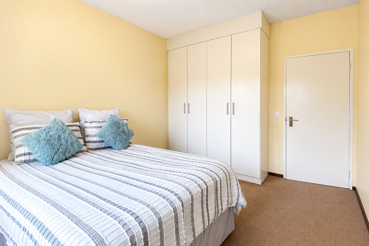 A bedroom featuring neutral walls, carpeted flooring, and a built-in wardrobe providing ample storage space.