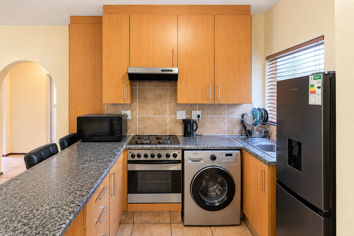 A functional kitchen featuring light wood cabinetry, granite countertops, a tiled backsplash, and integrated appliances including an oven, hob, and washing machine.