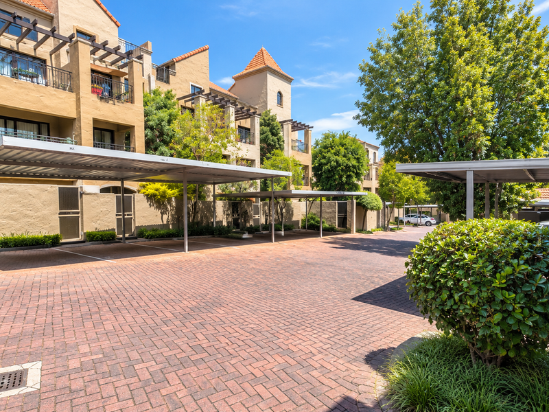 A well-maintained apartment complex exterior featuring paved parking areas, covered carports, and established landscaping.