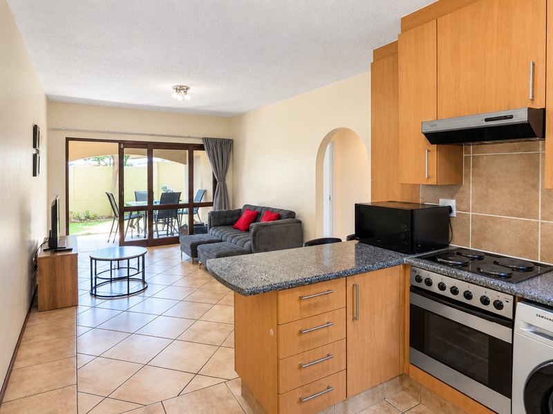 Open-plan living area featuring a functional kitchen with wood-finish cabinetry, granite countertops, and direct access to a private patio through sliding glass doors.