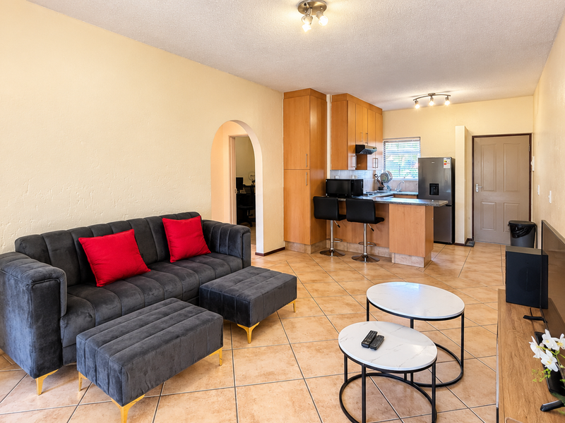 Open-plan living area featuring tiled flooring, a functional kitchen with breakfast bar, and a connecting archway leading to adjacent rooms.