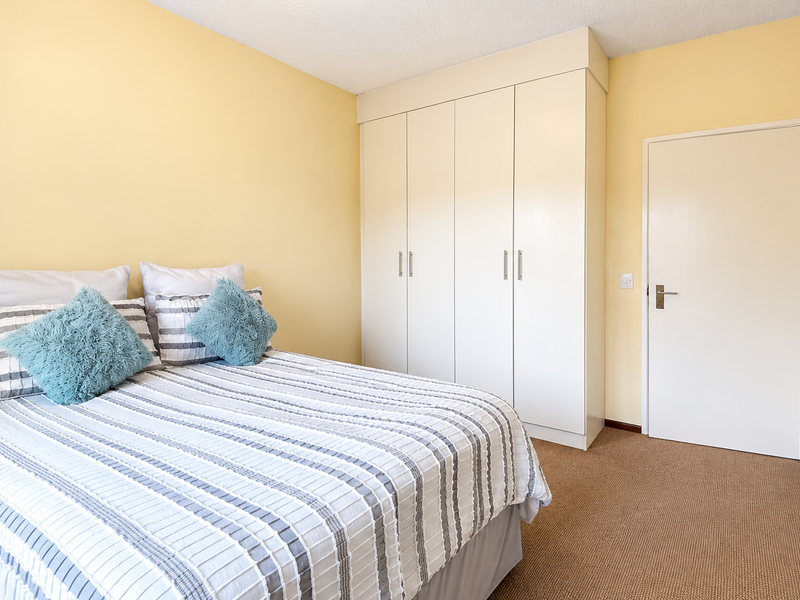 A bedroom featuring neutral walls, carpeted flooring, and a built-in wardrobe providing ample storage space.