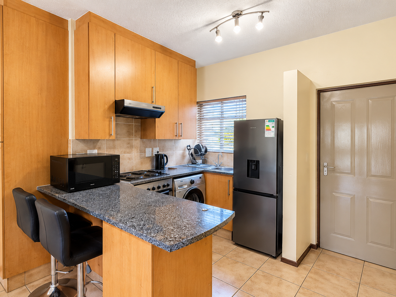 A functional kitchen featuring light wood cabinetry, granite countertops with a breakfast bar, tiled backsplash, and integrated appliances.