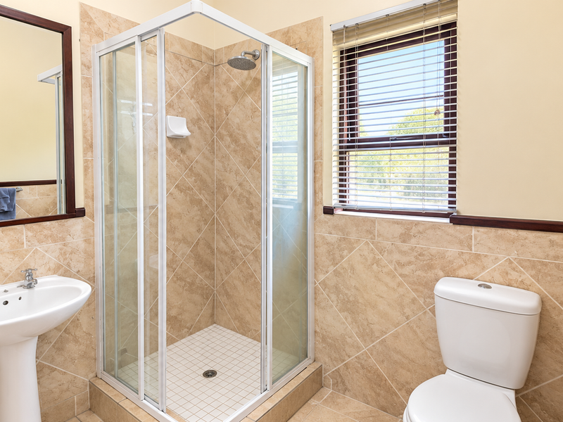 A clean and functional bathroom featuring a pedestal basin, a corner shower enclosure, and a toilet, finished with neutral wall and floor tiling.