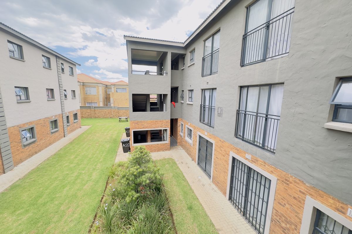 View of the apartment complex rear elevation featuring brick and plaster facade, balconies with railings, security bars, and a well-maintained communal garden area.