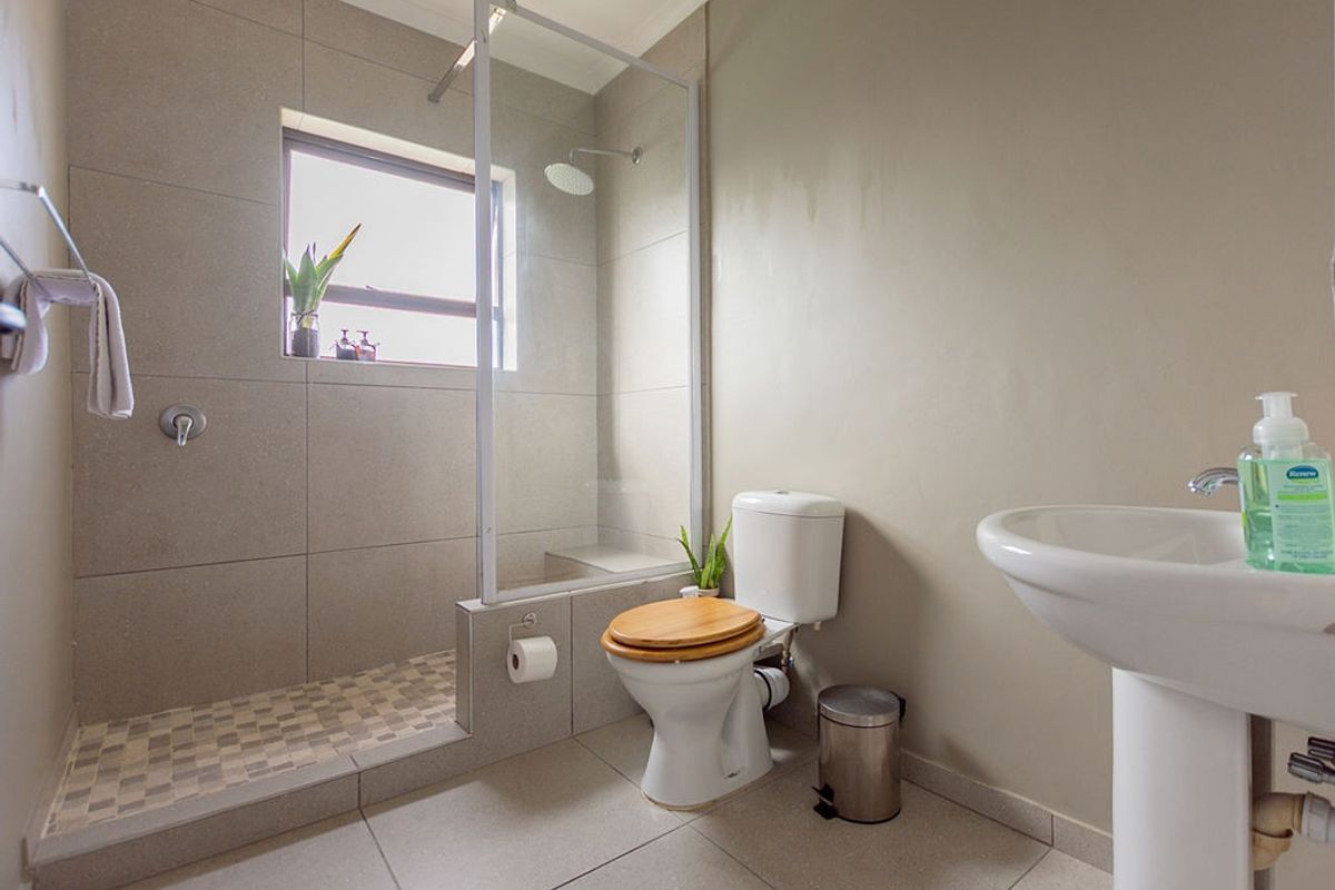 Modern bathroom featuring a walk-in shower with glass screen, pedestal basin, and tiled flooring.