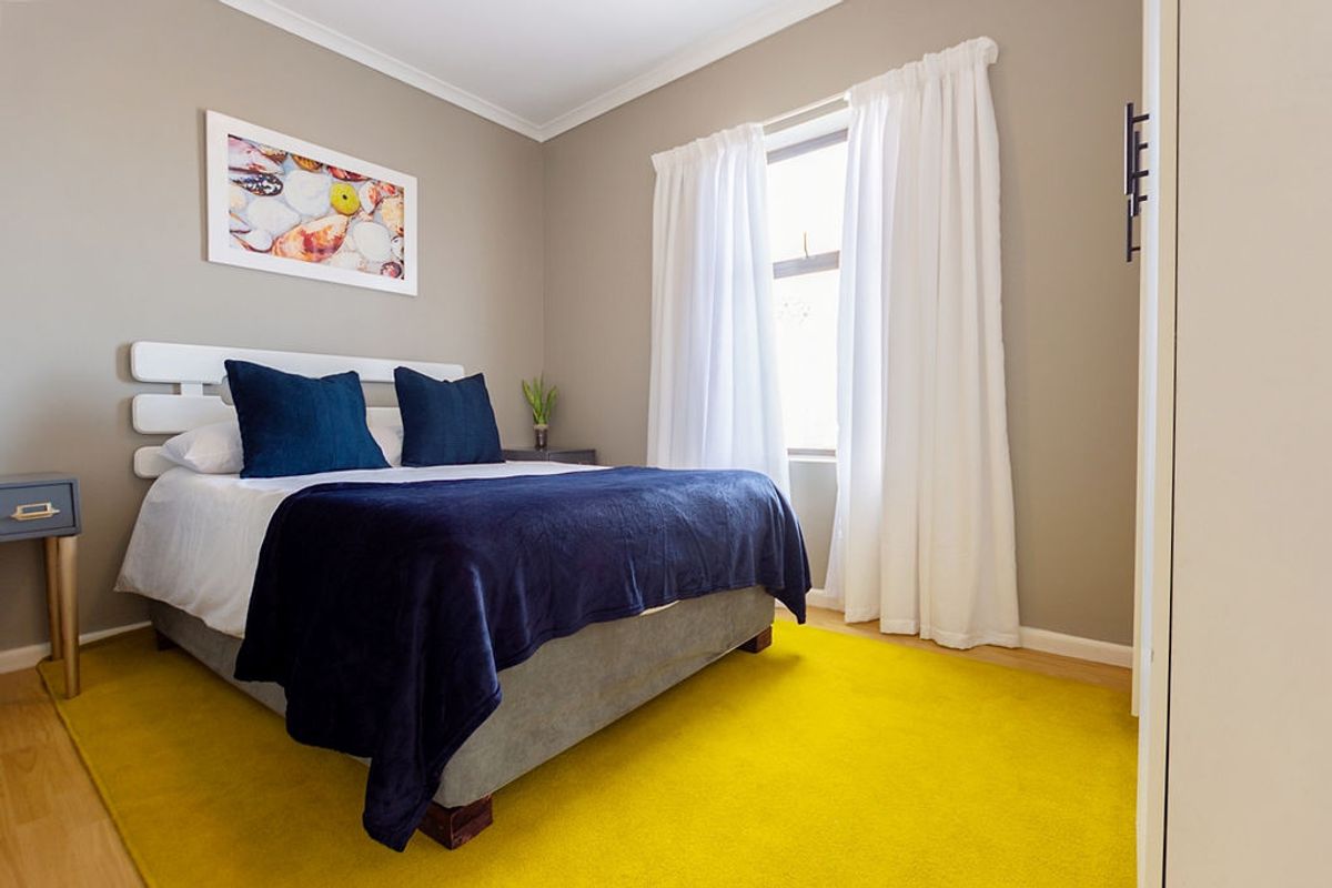 A well-maintained bedroom featuring neutral wall tones, laminate flooring, and a window with curtain tracks.