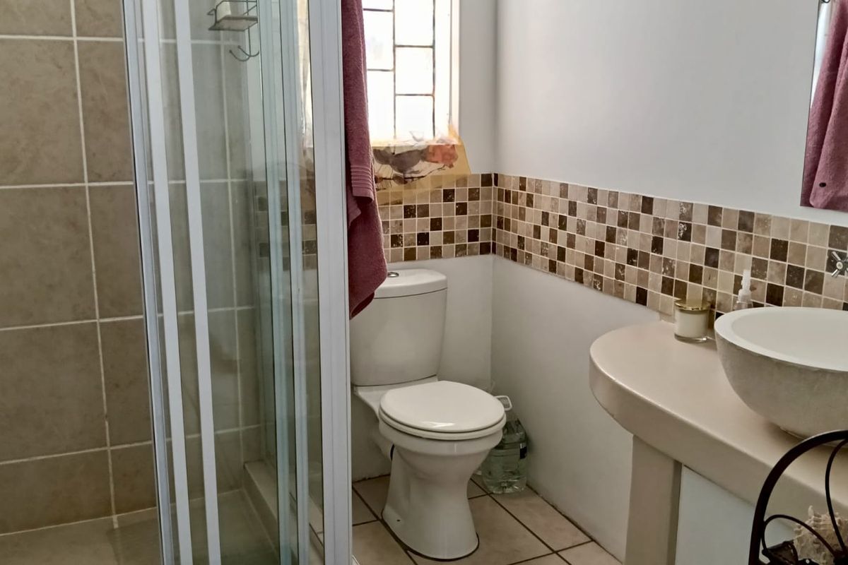 A functional bathroom featuring a glass-enclosed shower, a pedestal-mounted basin, and a standard toilet with neutral wall and floor tiling.