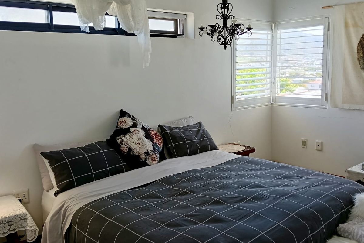 A cozy bedroom featuring corner windows with shutters, providing natural light and views, complemented by a decorative chandelier and high-level clerestory windows.