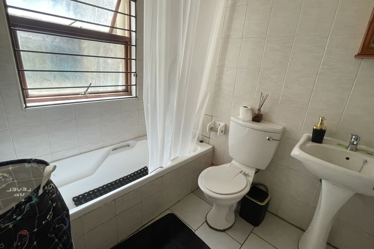 A compact bathroom featuring a bathtub with shower curtain, pedestal basin, and toilet, finished with neutral wall and floor tiles.
