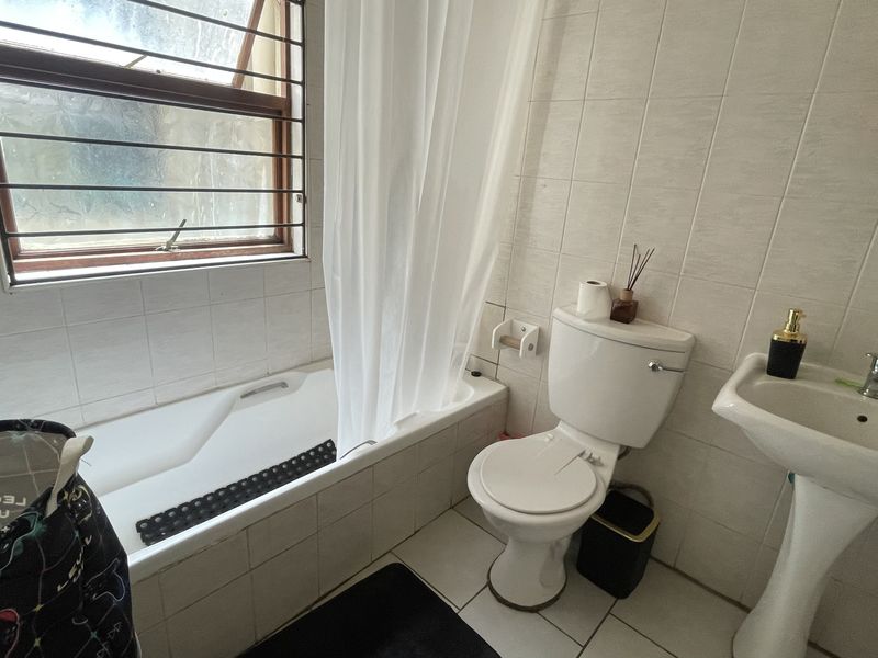A compact bathroom featuring a bathtub with shower curtain, pedestal basin, and toilet, finished with neutral wall and floor tiles.