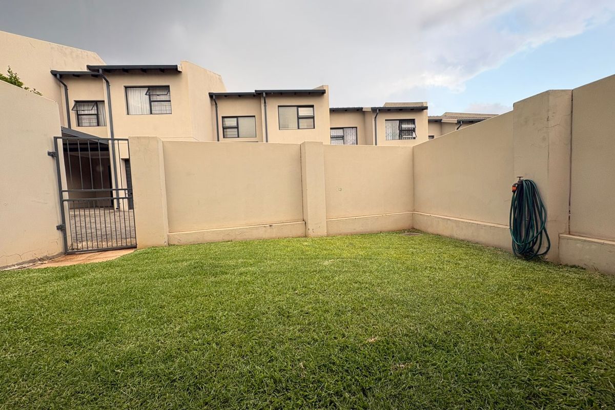 A private rear garden area featuring a well-maintained lawn, enclosed by high perimeter walls and a secure metal gate.