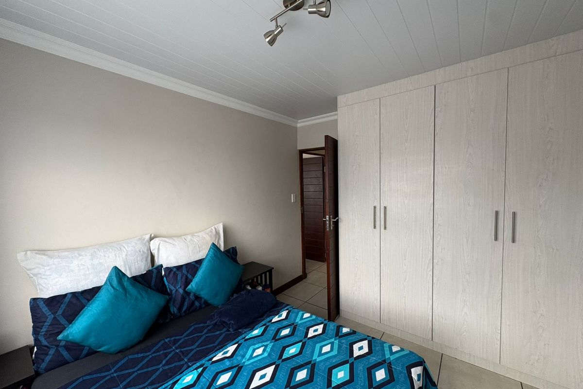 A well-maintained bedroom featuring built-in cupboards, tiled flooring, and a modern tongue and groove ceiling with a spotlight fixture.