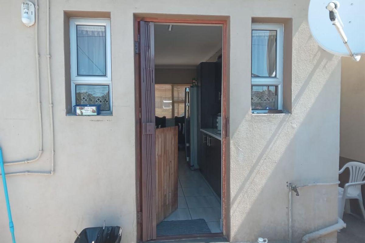 Rear exterior view of the townhouse showing a security gate entrance, aluminium windows, and exterior utility connections.