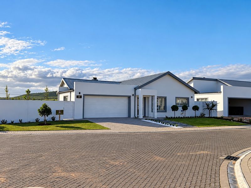 Modern single-story residential home featuring a clean white facade, paved driveway, double garage, and well-maintained landscaped front garden.