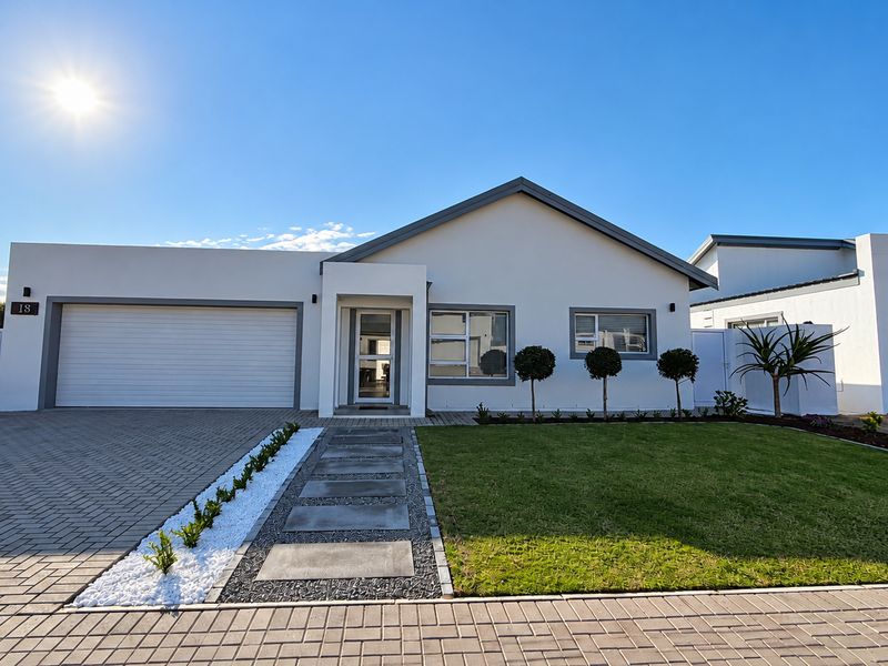 Modern single-story residential home featuring a paved driveway, automated garage, manicured front garden, and clean architectural lines.