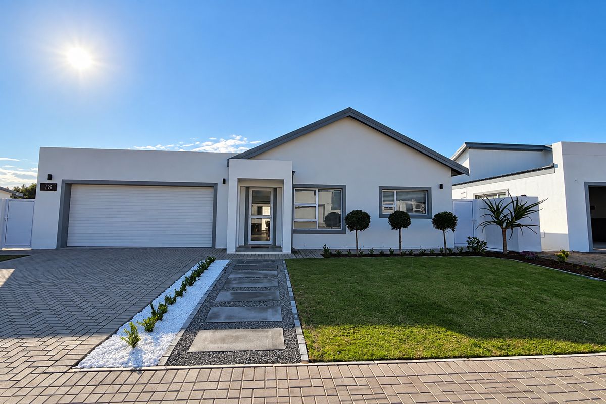 Modern single-story residential home featuring a paved driveway, automated garage, manicured front garden, and clean architectural lines.