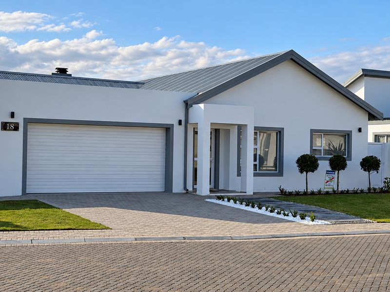 Modern single-story residential home featuring a clean white facade, grey metal roof, paved driveway, and a well-maintained front garden.