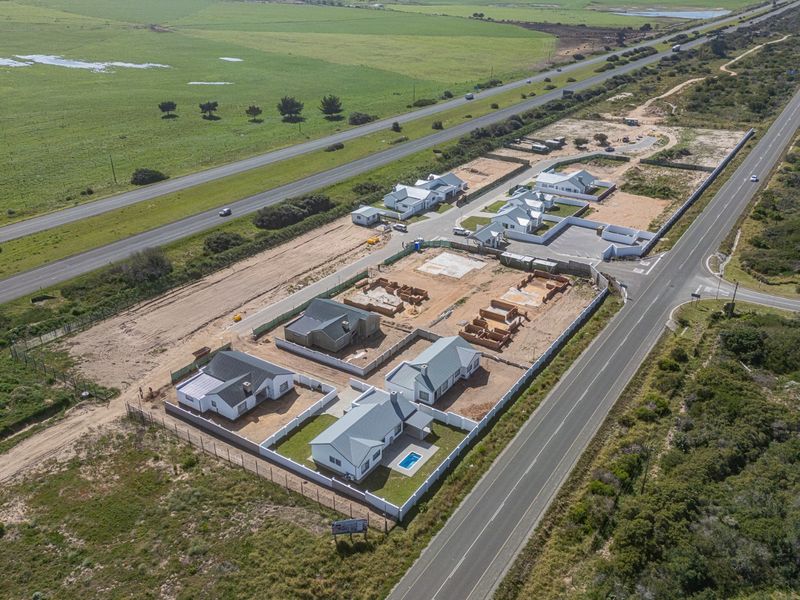 Aerial view of a residential development site showing multiple houses in various stages of construction, including completed units with pools and perimeter fencing.