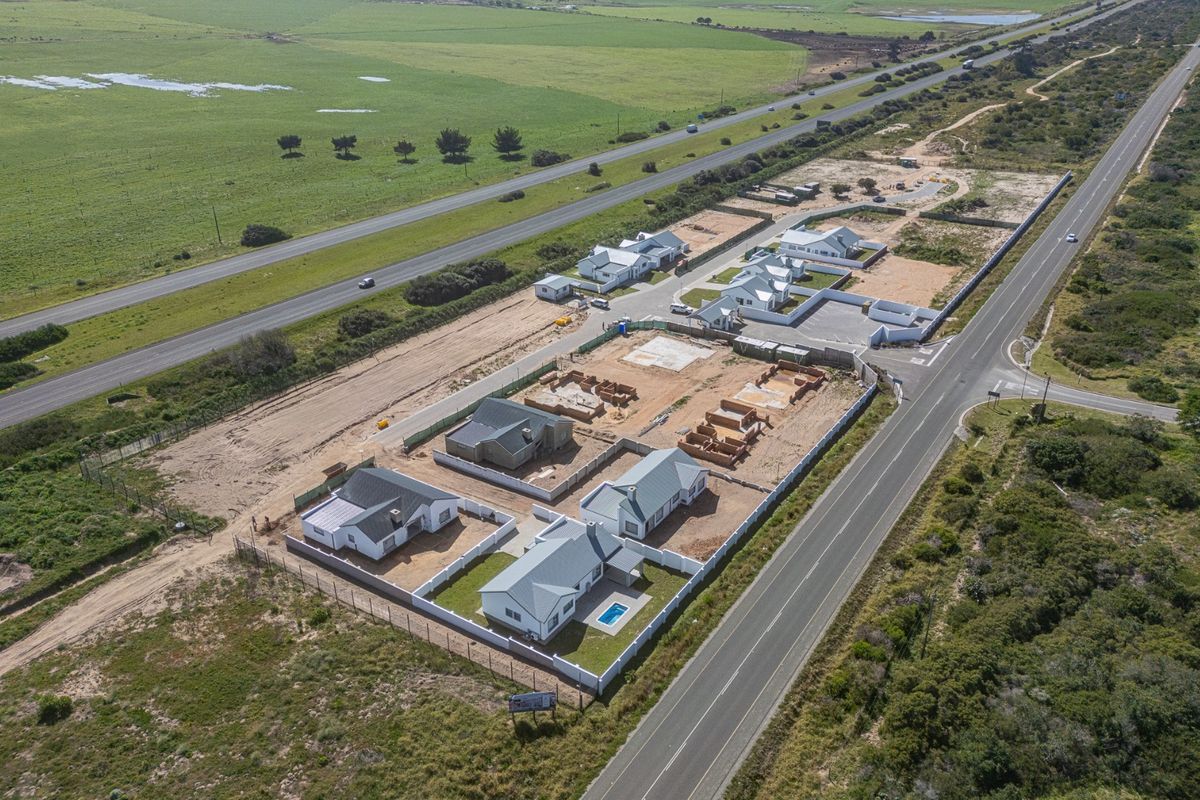 Aerial view of a residential development site showing multiple houses in various stages of construction, including completed units with pools and perimeter fencing.