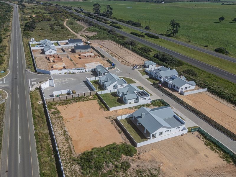 Aerial view of a residential housing development featuring multiple detached homes with metal roofs, perimeter walls, and paved access roads.