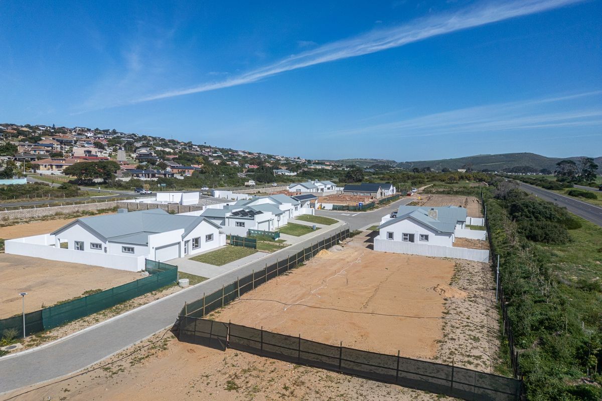Aerial view of a residential development featuring modern single-story homes with metal roofs, paved driveways, and surrounding undeveloped plots.