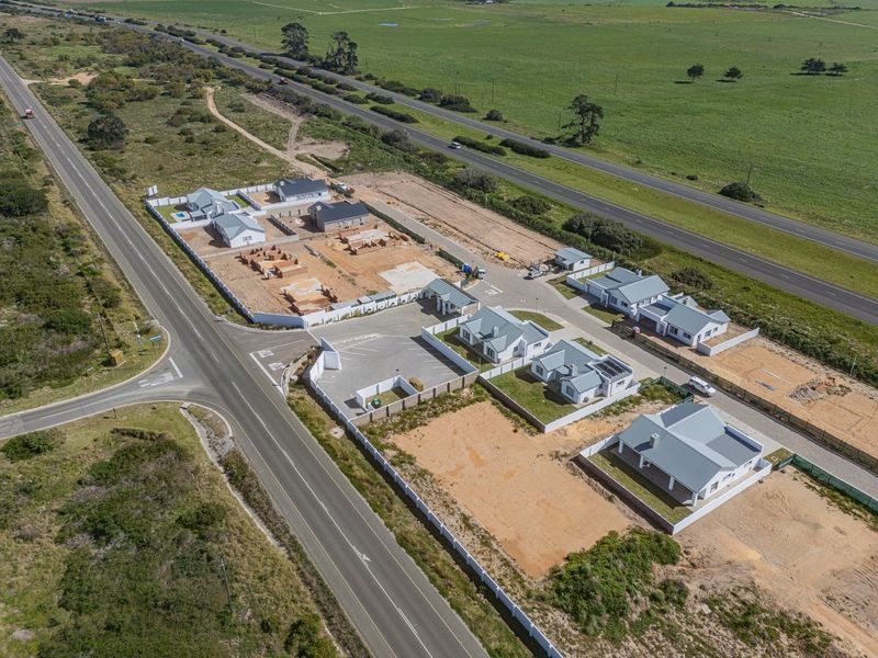 Aerial view of a residential development site featuring multiple detached houses, paved access roads, and perimeter fencing near a main highway.