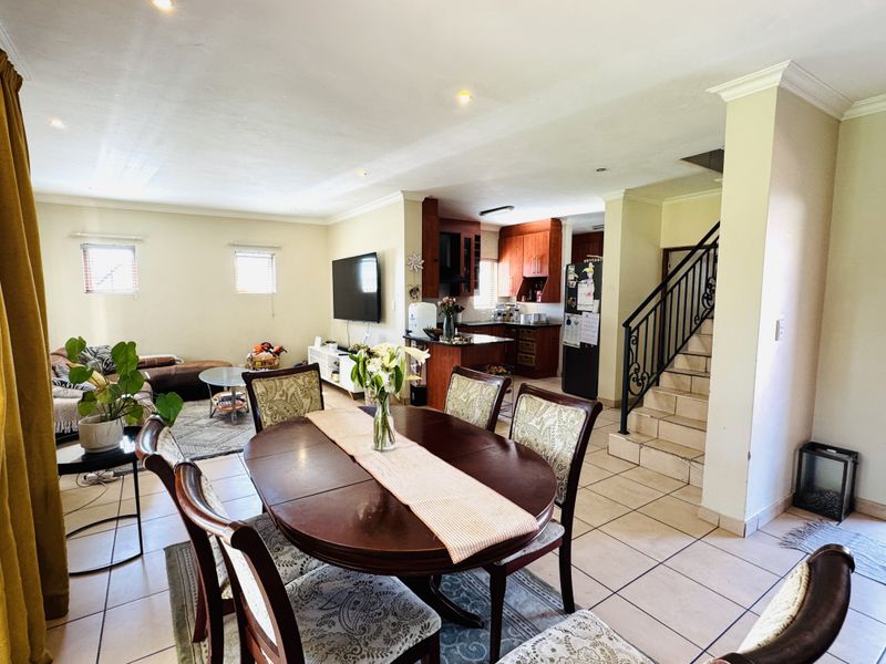 Spacious open-plan living and dining area featuring tiled floors, recessed lighting, and a functional kitchen with wooden cabinetry and a breakfast bar.