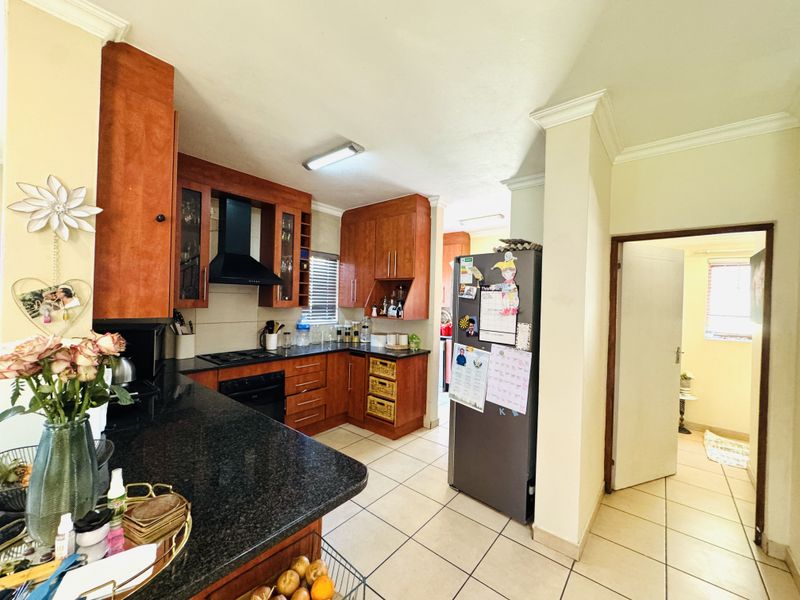 A functional kitchen featuring warm-toned wooden cabinetry, dark granite countertops, built-in cooking appliances, and tiled flooring, leading into an adjacent hallway.