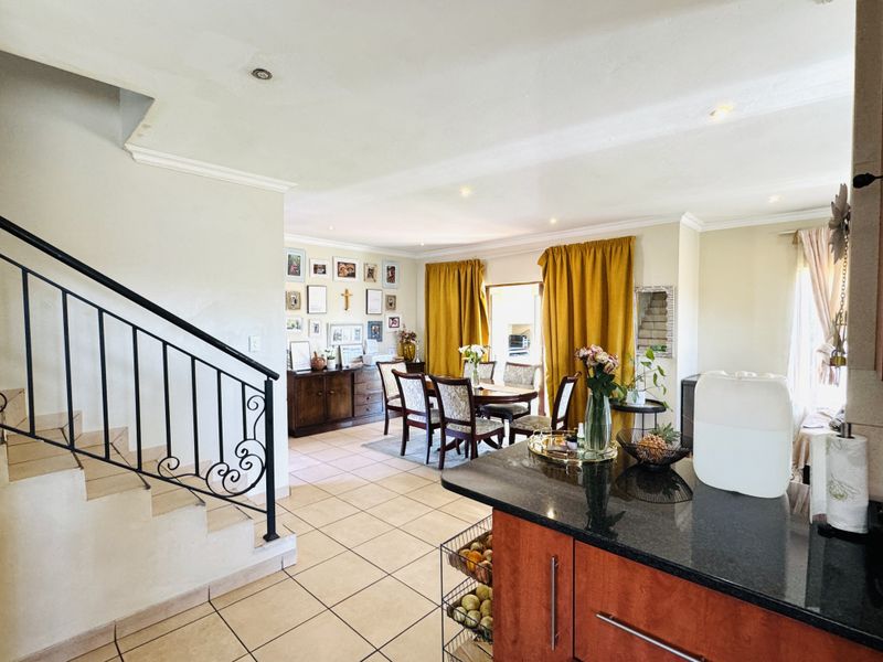 Open plan living and dining area featuring tiled floors, a wrought iron staircase, and a kitchen with granite countertops and built-in cabinetry.
