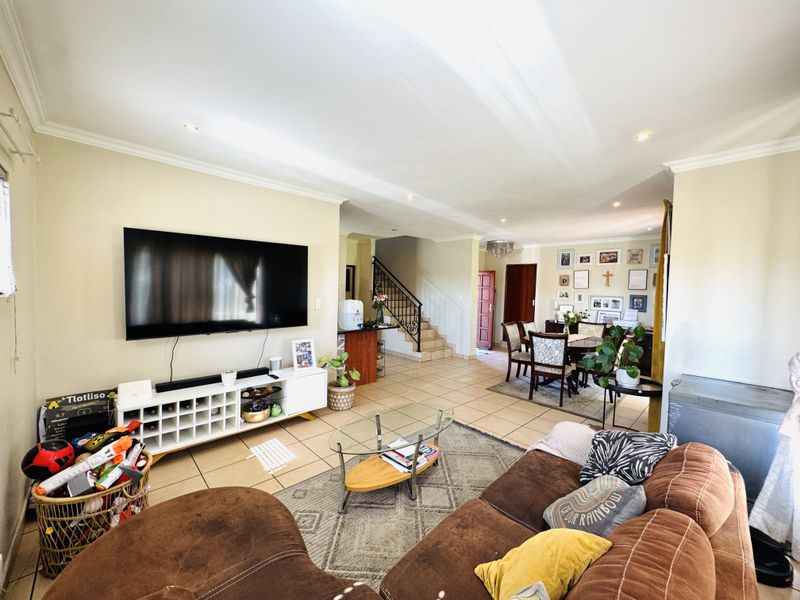 Spacious open-plan living and dining area featuring tiled flooring, recessed lighting, and a staircase with a decorative metal balustrade.