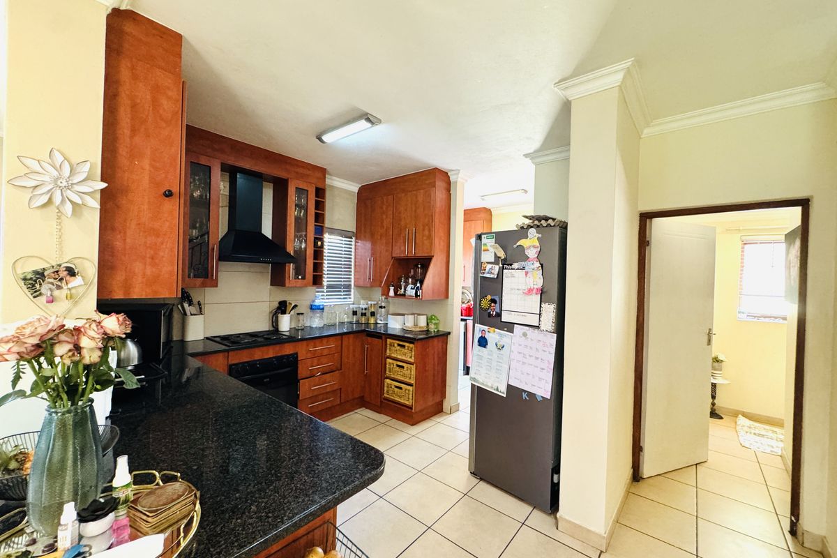 A functional kitchen featuring warm-toned wooden cabinetry, dark granite countertops, built-in cooking appliances, and tiled flooring, leading into an adjacent hallway.