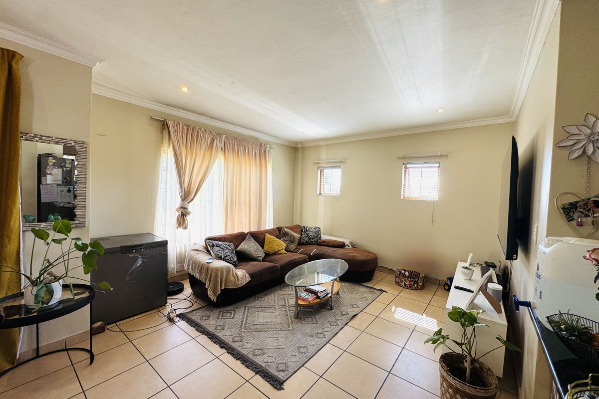 A spacious living room featuring neutral tiled flooring, recessed ceiling lighting, and coved cornicing, providing a functional and well-lit area for relaxation.