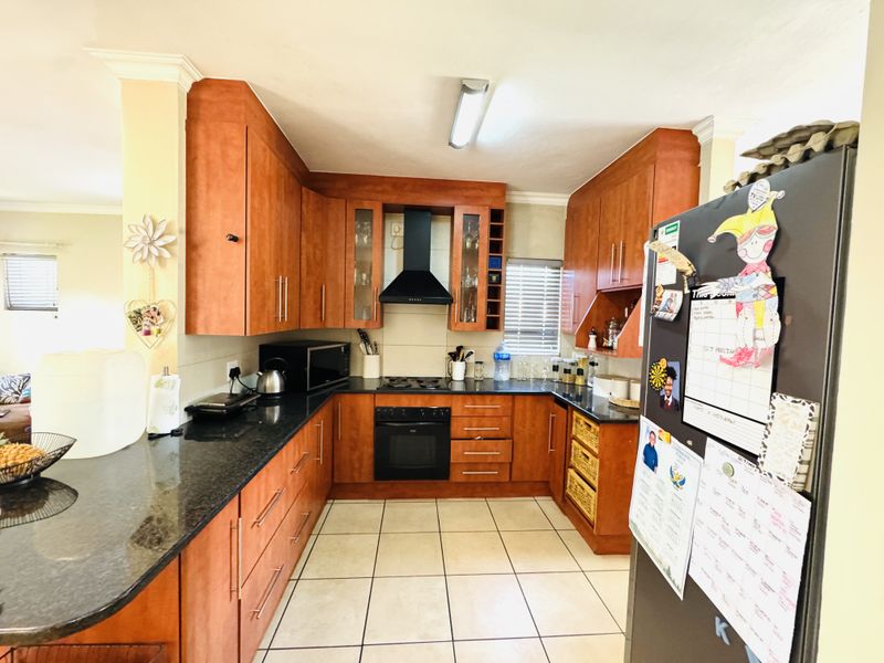 A functional kitchen featuring warm-toned wooden cabinetry, granite countertops, a built-in oven with gas hob, and tiled flooring.