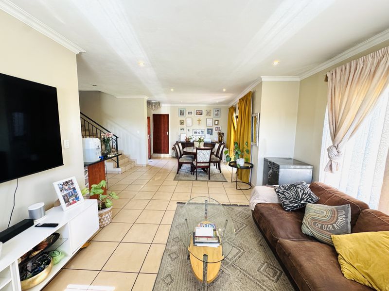 Spacious open-plan living and dining area featuring neutral tiled flooring, recessed lighting, and a staircase leading to the upper level.