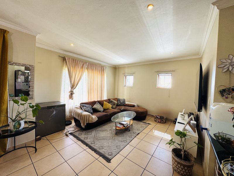 A spacious living room featuring neutral tiled flooring, recessed ceiling lighting, and coved cornicing, providing a functional and well-lit area for relaxation.