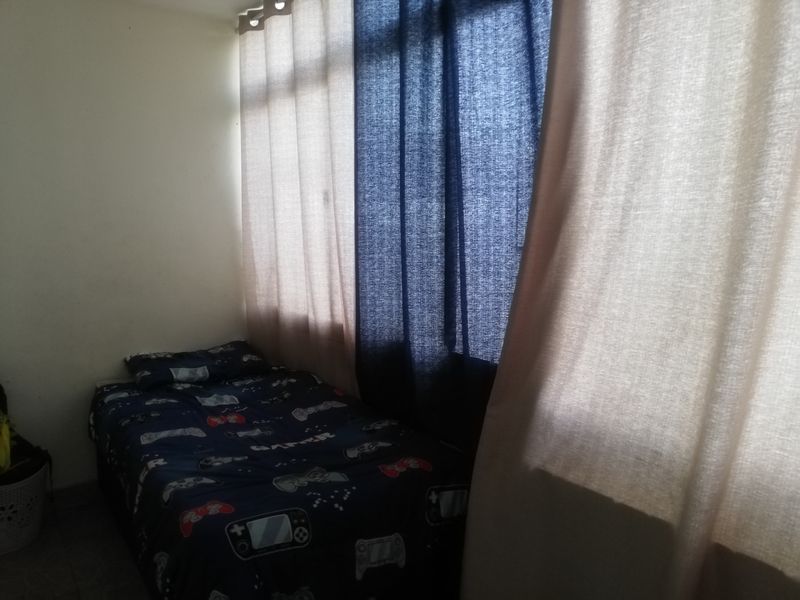 A bedroom featuring large windows covered by curtains, providing natural light to the space.