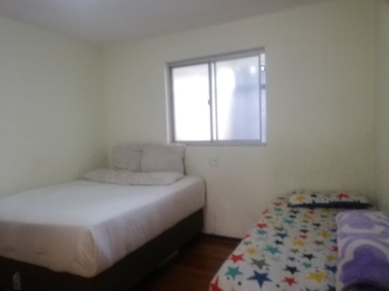A functional bedroom featuring wooden flooring and a sliding window, providing a simple and practical living space.