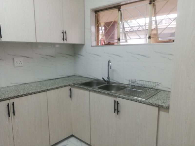 A functional kitchen area featuring light wood-grain cabinetry, granite-look countertops, a double stainless steel sink, and marble-effect wall tiling.