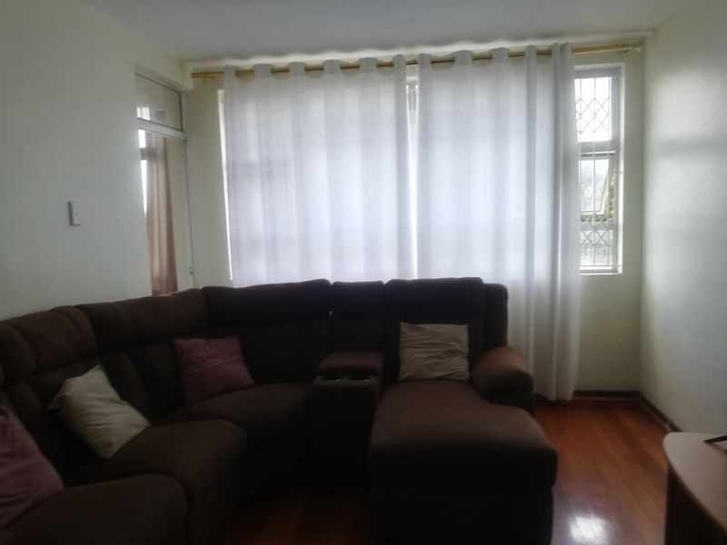 A living room featuring polished timber flooring and large windows covered by floor-to-ceiling curtains, providing natural light to the space.