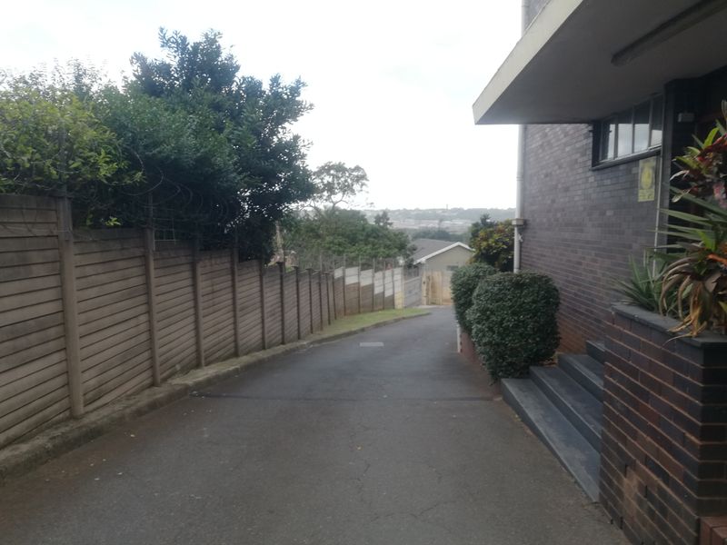 A view of the property driveway and side access, featuring brick exterior walls, concrete steps, and a perimeter boundary wall.
