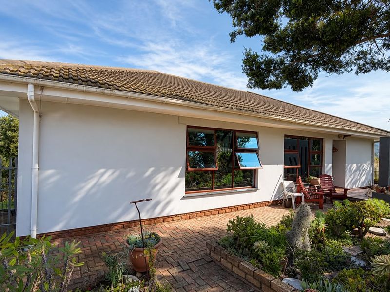 A well-maintained rear exterior view of the house featuring brick paving, a tiled roof, and established garden beds.