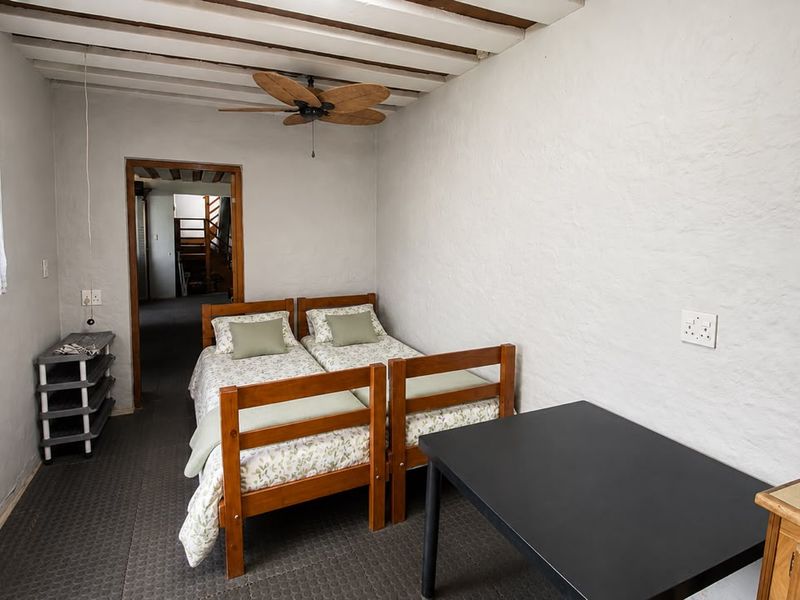 A bedroom featuring textured walls, an exposed beam ceiling, and a ceiling fan, offering a rustic aesthetic with potential for modern updates.