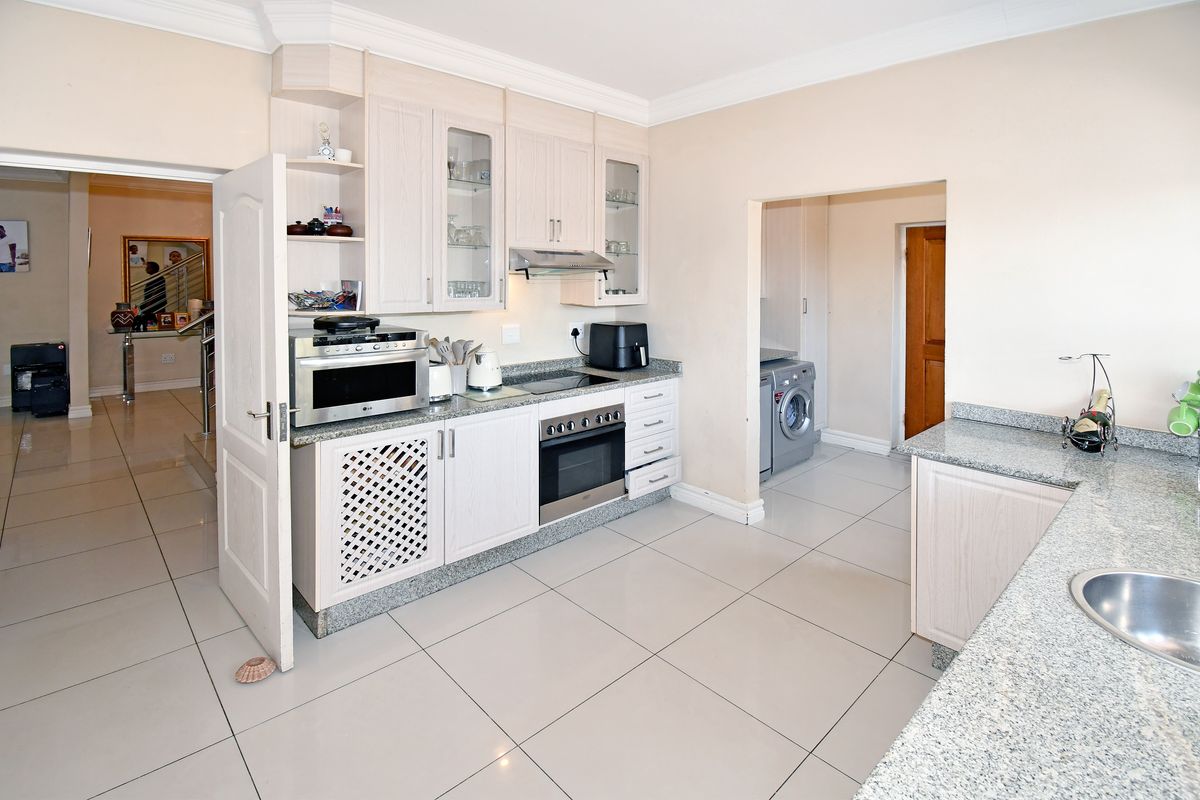 A functional kitchen featuring light wood-finish cabinetry, granite countertops, integrated oven and hob, and tiled flooring, with an adjacent laundry area.