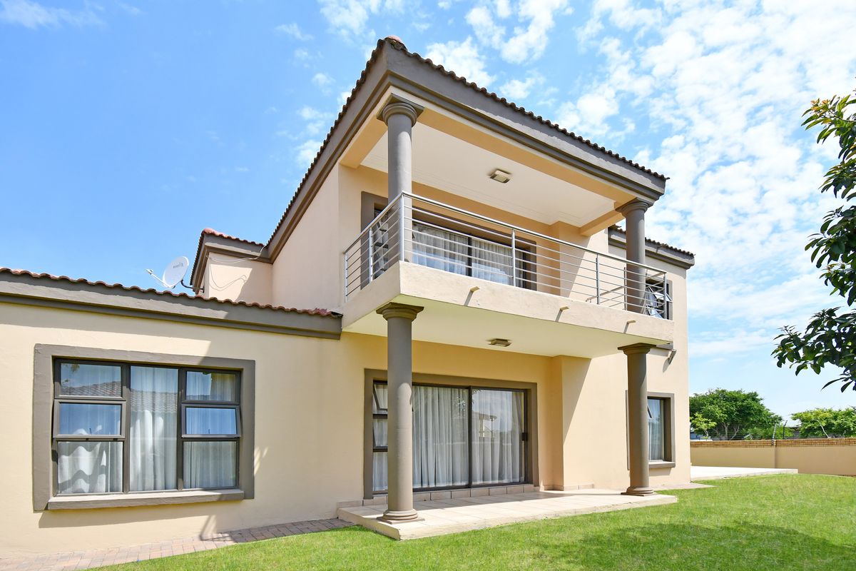 Rear view of a double-story house featuring a covered patio, a spacious upper-level balcony with stainless steel railings, and a well-maintained garden.