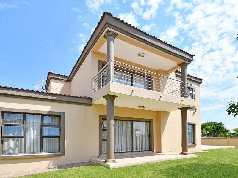 Rear view of a double-story house featuring a covered patio, a spacious upper-level balcony with stainless steel railings, and a well-maintained garden.